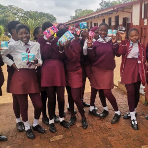 Young girls in school uniform holding up packages of sanitary pads